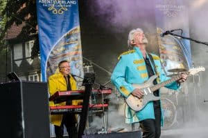 Abenteuerland Coverband live auf der Bühne, mit LED-Backdrops, in bunten Kostümen, rockt beim Musikfestival, steht vor Banner, bei Abendveranstaltung, repräsentiert professionelle Coverband-Performance.