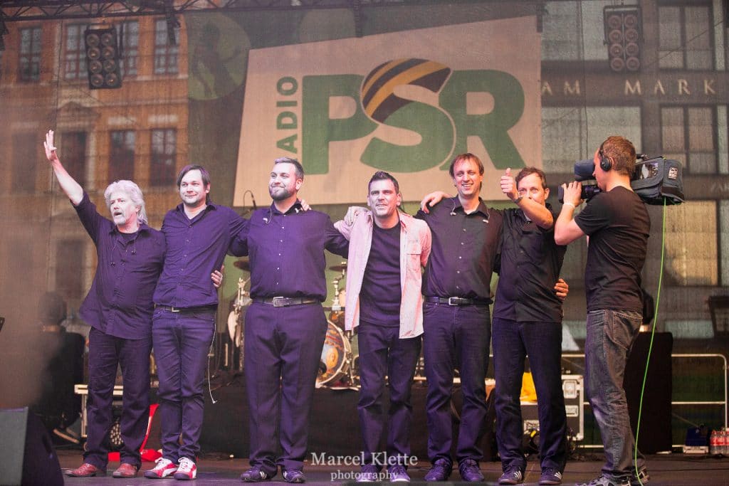 Abenteuerland Coverband auf der Bühne beim Live-Konzert, mit Bandmitgliedern, die sich für den nächsten Auftritt bedanken, im Hintergrund das Abenteuerland Logo und die Radio PSD Werbung, stimmungsvolle Musikveranstaltung.