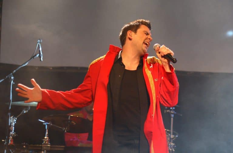 Mitreißender Sänger in rotem Bühnenoutfit beim Abenteuerland Coverband Konzert, Live-Performance auf der Bühne im Event, emotionale Stimmung, musikalisches Highlight bei der Bandreise.