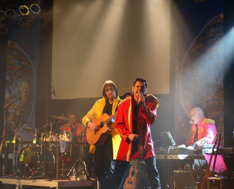 Mitreißende Coverband auf der Bühne bei einem Abenteuerland-Konzert in einem festlichen Event, leidenschaftliche Musiker mit Gitarren, Schlagzeug und Mikrofon, bunte Kostüme, kreative Bühnen-Atmosphäre, perfekte Unterhaltung für Events, Festivals, Hochzeiten.