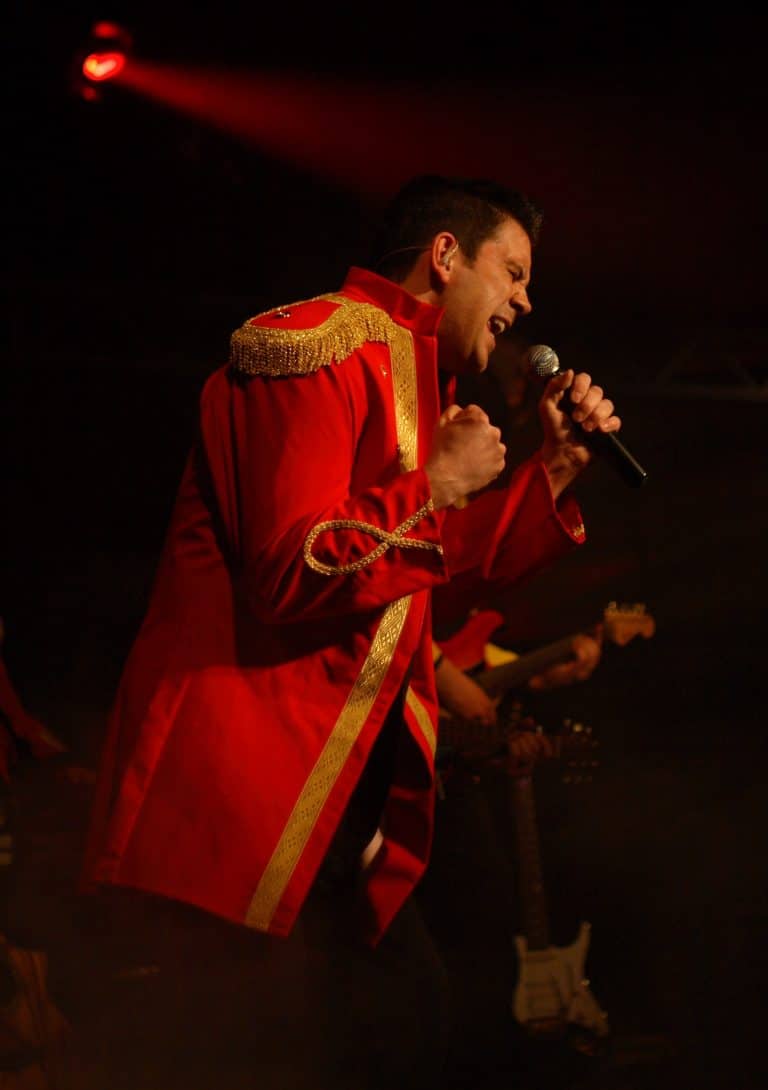 Hochwertiger Live-Auftritt der Coverband Abenteuerland, energisch singend im roten Bühnenoutfit, mit Gitarristen im Hintergrund. Perfekt für Events, Hochzeiten und Festivals.