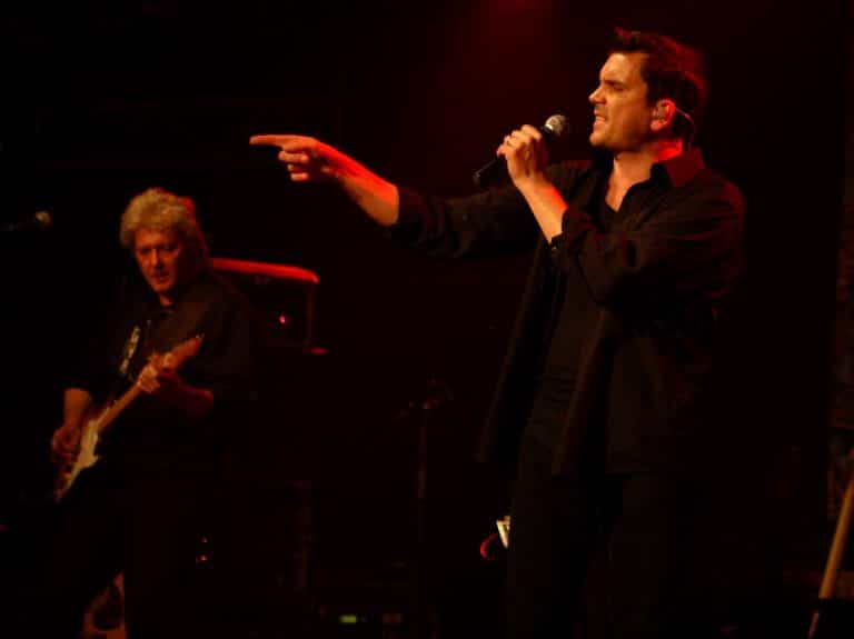 Emotionally expressive male singer performing live on stage with guitarist in the background, vibrant red lighting, during Abenteuerland event.