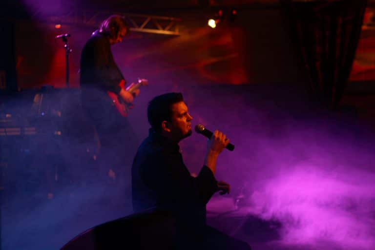 Mitreißende Coverband-Performance bei Abenteuerland: Sänger im Dunkeln mit Mikro, im Hintergrund Gitarrist, geheimnisvolle Lichteffekte schaffen ein einzigartiges Live-Erlebnis.