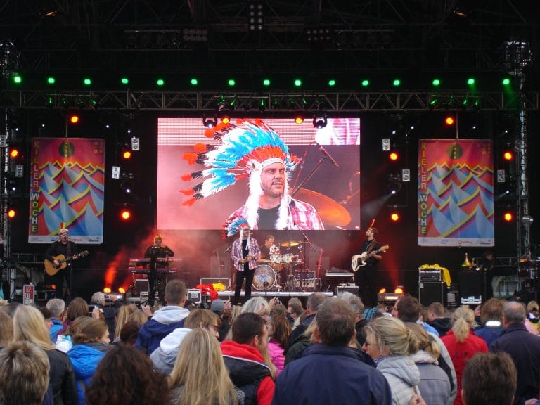 Abenteuerland Musikband beim Open-Air-Konzert auf der Kieler Woche, vibrant auf der Bühne mit großem LED-Bildschirm, Publikum genießt live Unterhaltung, festlicher Musikauftritt.