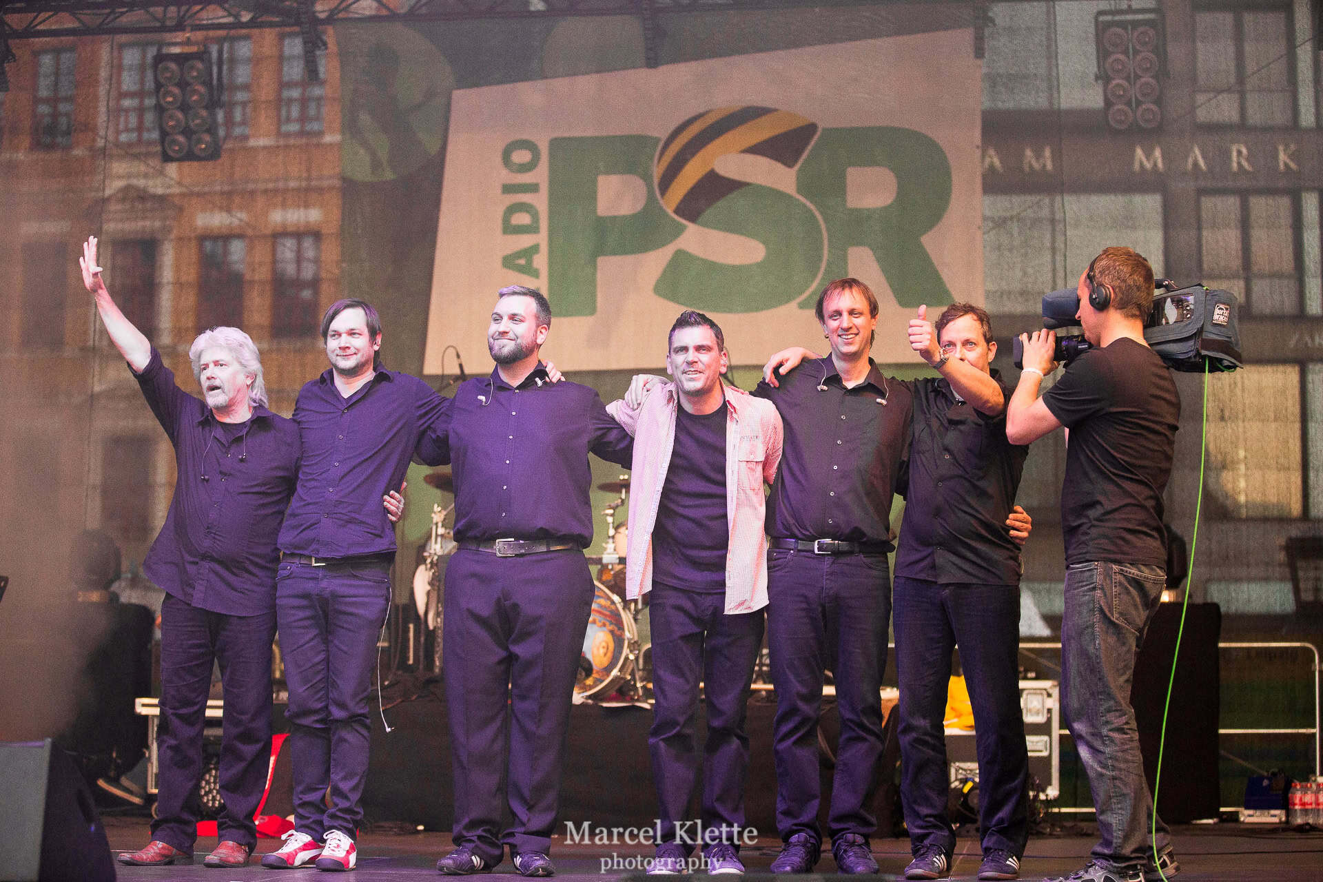Abenteuerland Coverband auf der Bühne beim Live-Konzert, mit Bandmitgliedern, die sich für den nächsten Auftritt bedanken, im Hintergrund das Abenteuerland Logo und die Radio PSD Werbung, stimmungsvolle Musikveranstaltung.