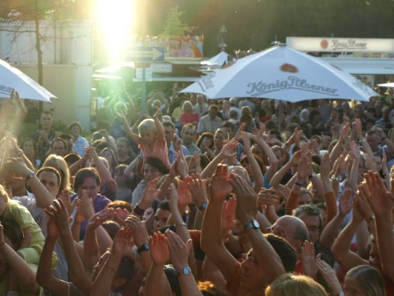 Abenteuerland Festival Publikum bei Konzert, ausgelassene Stimmung, Sonne, Sonnenuntergang, Freizeitpark, Musik-Event, Gemeinschaft, Familienunterhaltung, Open-Air, Sommer, Live-Musik, Festivalatmosphäre, Kinder und Erwachsene, feiern, outdoor Erlebnis.