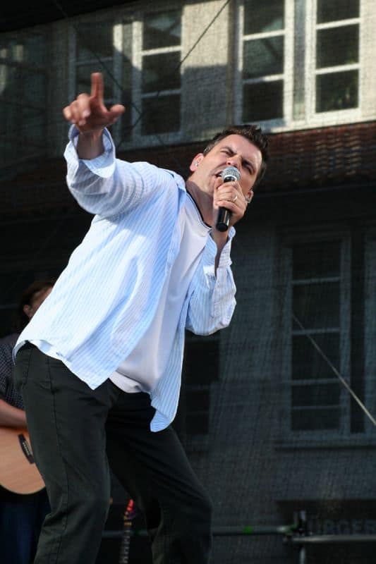Dynamischer Sänger der Coverband Abenteuerland bei einem Auftritt auf der Bühne, singt leidenschaftlich ins Mikrofon und begeistert das Publikum.