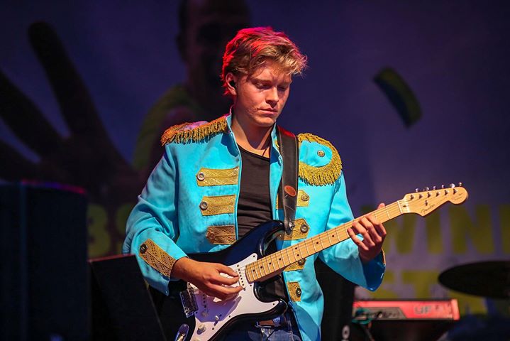 Stimmungsvoller Musiker in bunter Zirkusjacke spielt E-Gitarre auf einer Bühne bei Abenteuerland Event.
